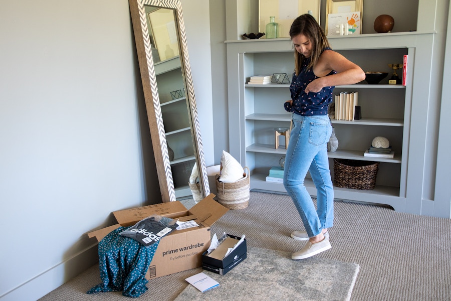 A woman trying on clothes in her home with an amazon prime wardrobe box near by