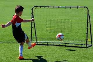 child kicking ball into net