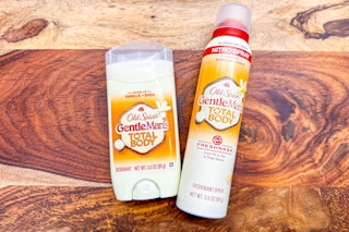 Orange colored Old Spice Total Body deodorant stick and dry spray bottle on a wood background