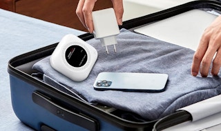 a carbon monoxide detector, plug, and phone on top of clothes in a suitcase