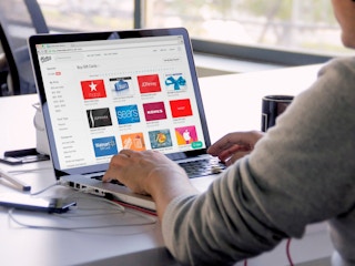 A person sitting at a table looking a a laptop open to raise.com website.