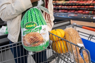 A woman putting a frozen turkey into a shopping cart.