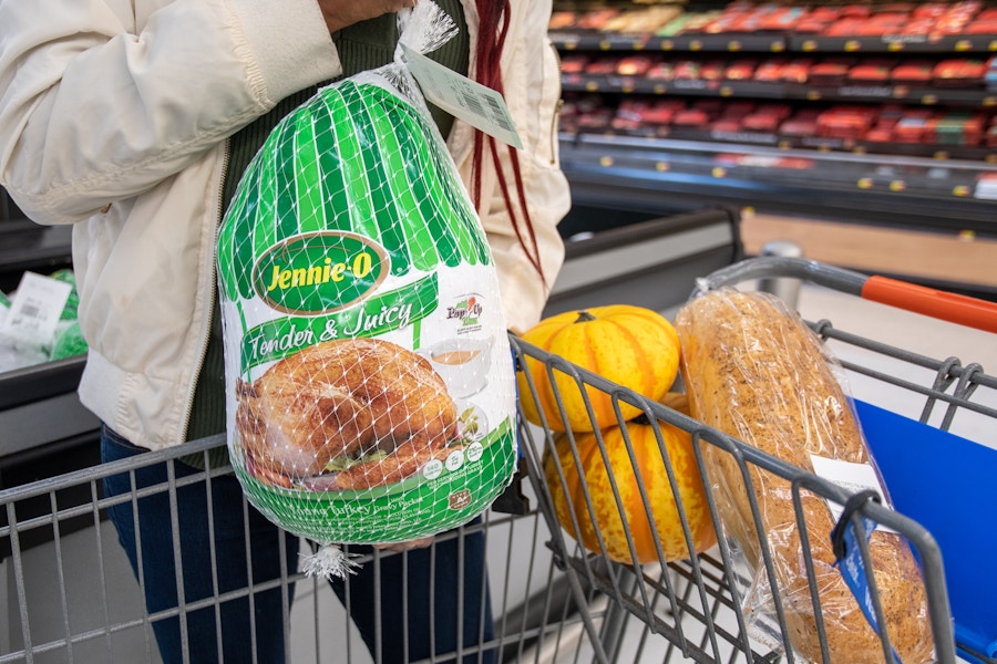 A woman putting a frozen turkey into a shopping cart.