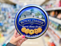 a hand holding a blue tin of cookies in a store aisle