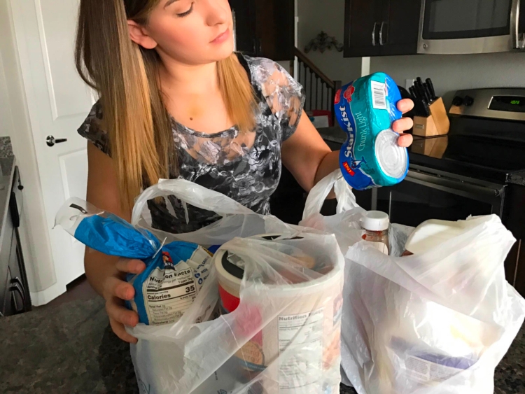 Woman removing groceries from plastic bags in a kitchen