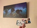 painting on the wall and someone holding up a card and stickers in front of it