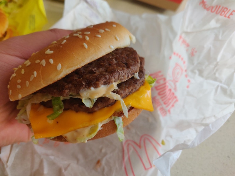 A person's hand holding a burger from McDonald's above the paper wrapper on the table.