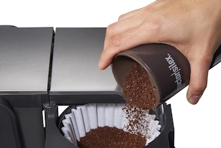 a person pour coffee grounds in a coffee maker