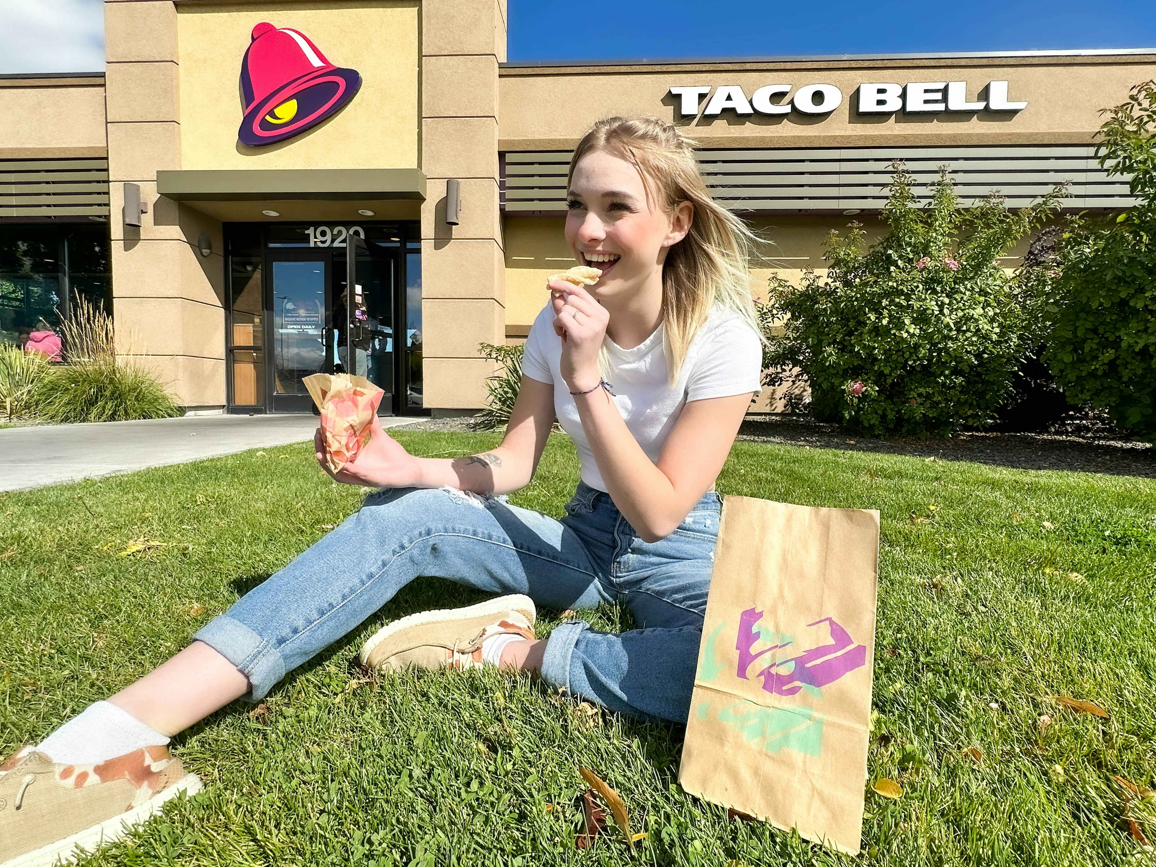 a person sitting in the grass outside taco bell eating cinnamon twists 