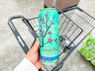hand holding arizona green tea with ginseng over a walgreens cart