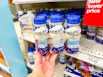 hand holding a 6-pack of ensure nutrition shake in front of a target shelf