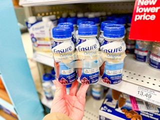 hand holding a 6-pack of ensure nutrition shake in front of a target shelf