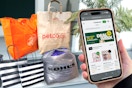 someone holding a phone showing the instacart deal week page online and bags from several retailers