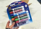 A hand holding a 12-pack of Expo dry erase markers.