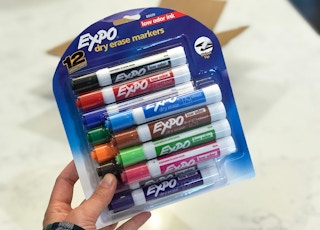 A hand holding a 12-pack of Expo dry erase markers.
