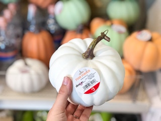 hand holding out small fake pumokin in front of pumpkin display at Target