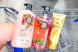 hand holding herbal essences and pantene hair care products over a shopping cart