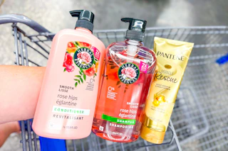 hand holding herbal essences and pantene hair care products over a shopping cart