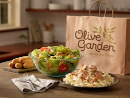 A large salad, breadsticks, and a pasta entree on a table in front of an Olive Garden bag