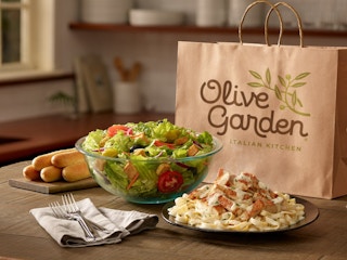 A large salad, breadsticks, and a pasta entree on a table in front of an Olive Garden bag