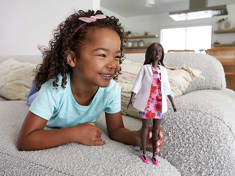 young girl playing with barbie doctor doll at home