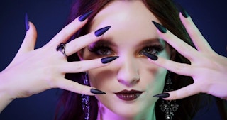 a woman holding her hands in front of her face with long dark fingernails