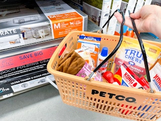A hand basket full of products held next to boxed dog crates at Petco