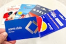 a person holding up a sams club gift card in front of various travel gift cards 