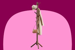A brown coat tree with 8 hooks and a tan trench coat and hat and brown purse hanging on it