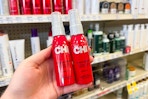 person holding 2 chi thermal heat spray bottles in front of the display shelves