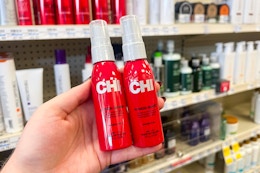 person holding 2 chi thermal heat spray bottles in front of the display shelves