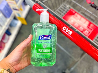 hand holding a bottle of Purell hand sanitizer in front of cVS cart