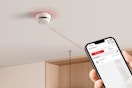 a smoke detector on a ceiling being controlled by a smartphone 