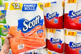 hand holding a pack of toilet paper in front of paper towels