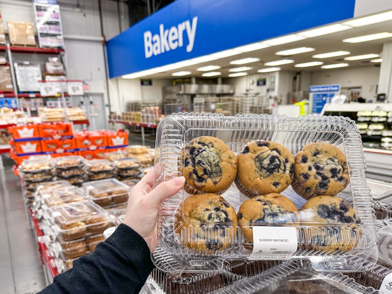 Someone holding up a case of blueberry muffins at the Sam's Club bakery