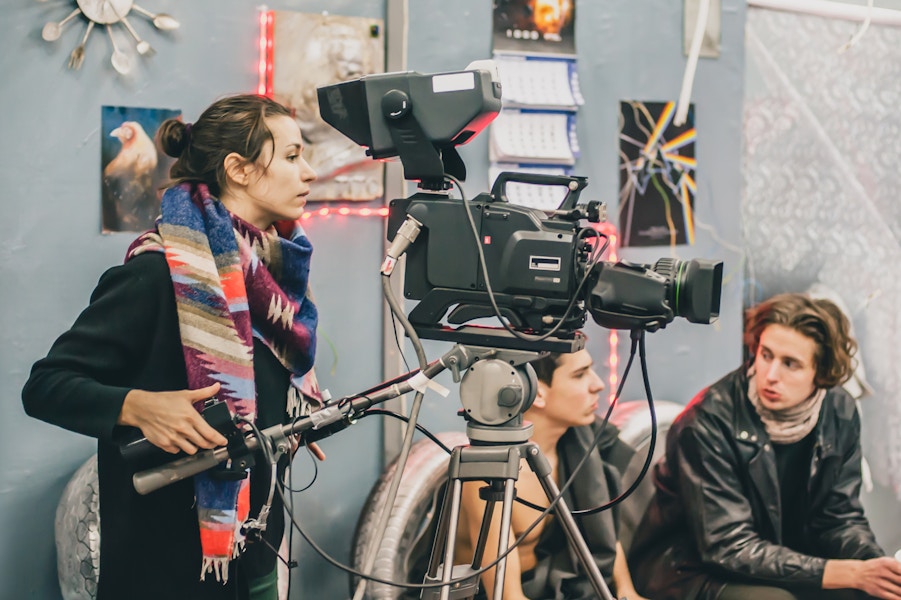 A person operating a camera while two other people sit in the background.