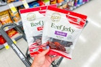 person holding 2 bags of beef jerky over a cart
