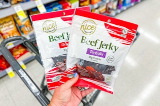 person holding 2 bags of beef jerky over a cart