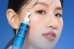 woman holding eye cream bottle to face