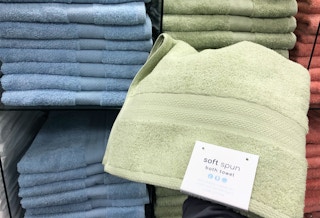 A Sunham soft spun bath towel being held in front of a display of them at Macy's.