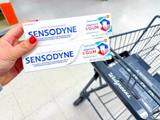 person holding 2 sensodyne toothpastes over a walgreens cart