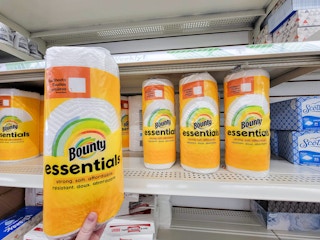 hand holding a roll of bounty essentials paper towels by other rolls of bounty paper towels