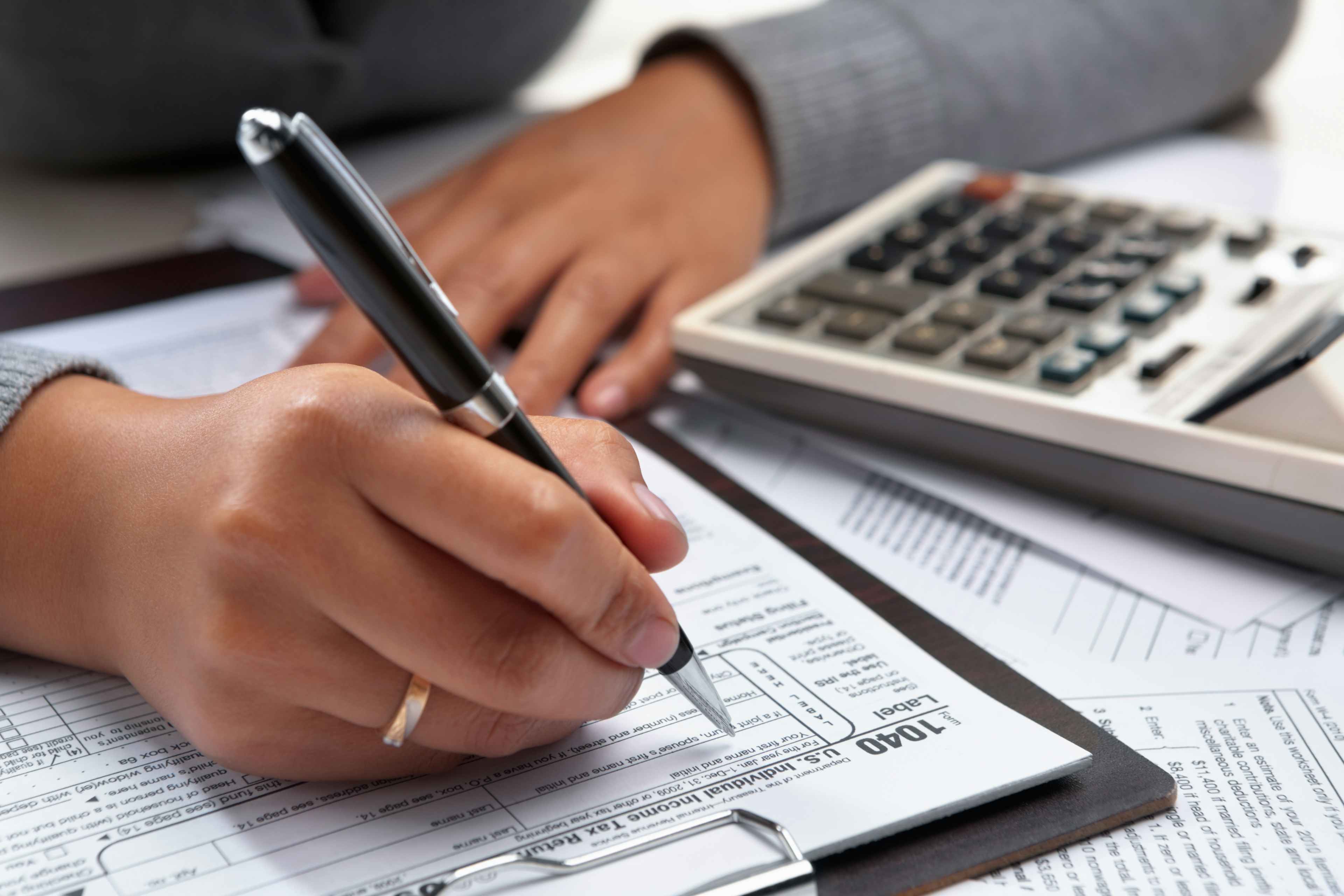 A person filling out a 1040 tax form with a calculator on the desk.