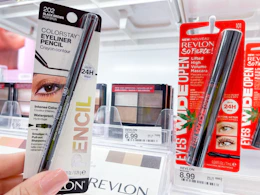 A Revlon eye liner package held out by hand in front of a Revlon eyeshadow and mascara.