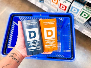 hand holding two duke cannon deodorants over walmart hand cart