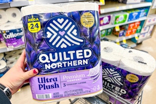 a hand holding a pack of toilet paper in a store over a buggy