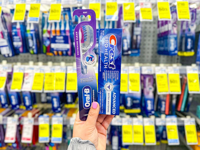 person holding crest toothbrush and toothpaste in front of the display