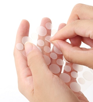 A person pulling a pimple patch off of a sheet.