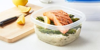 a food container with salmon and rice next to a cutting board
