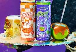 Two orange and purple cans of energy drinks next to a caramel apple and Halloween colors